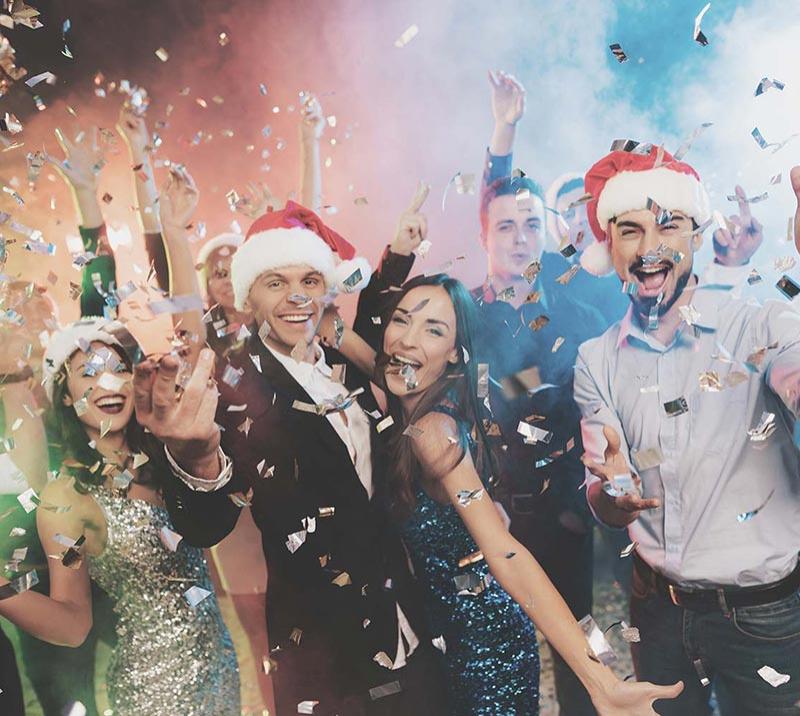Christmas guests in Santa hats pose for the camera as confetti falls from the ceiling.