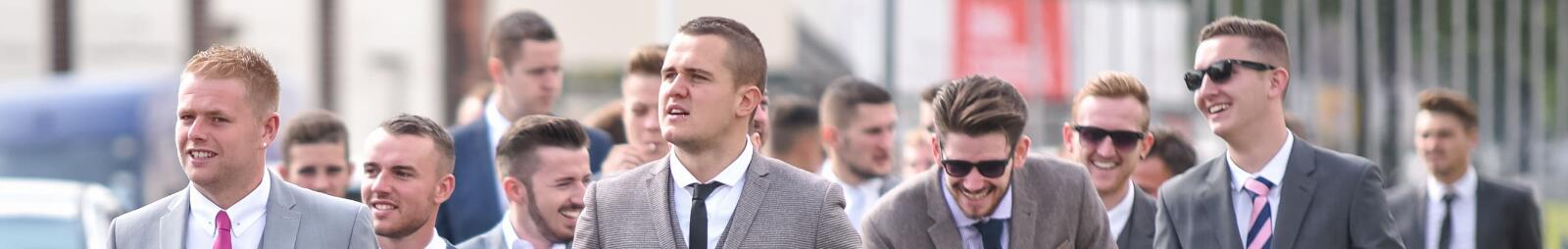 A large group of guys in suits heading towards the racecourse