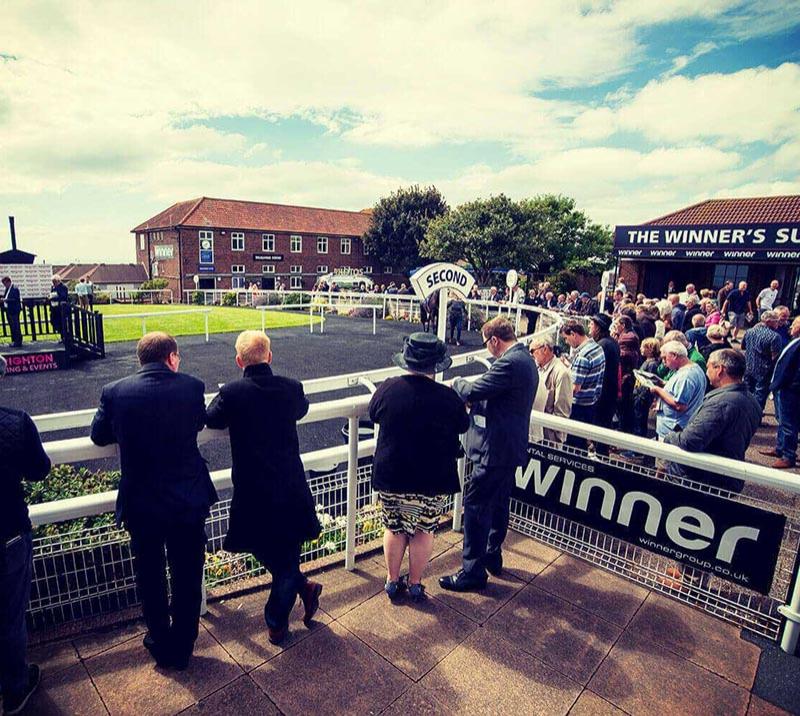 A crowd wait to see the horses and jockeys around the parade ring.